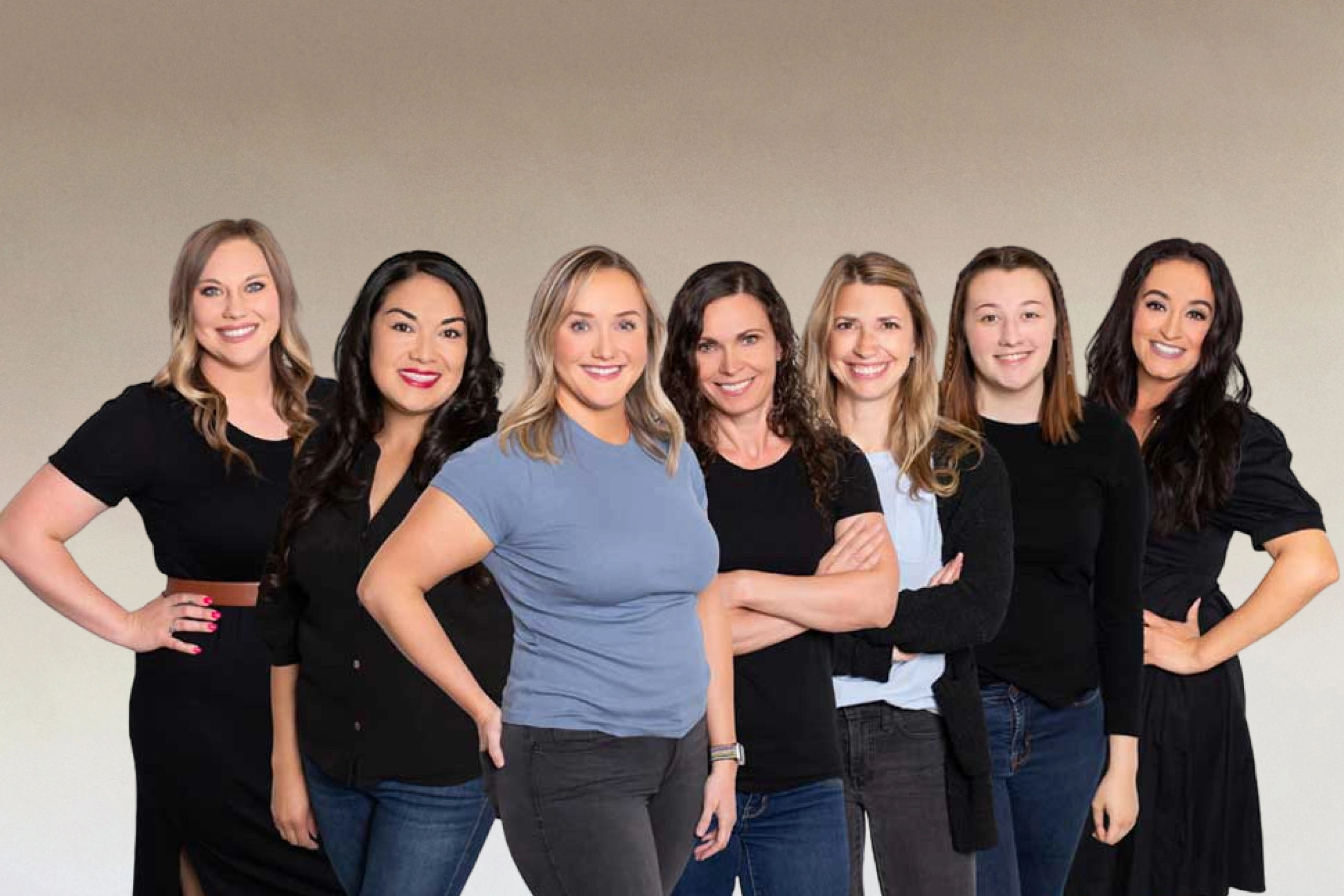 Seven women dental professionals standing together in casual poses against neutral background.