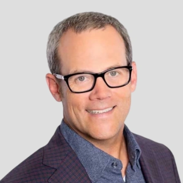 Professional headshot of man wearing glasses and blue shirt against neutral background.