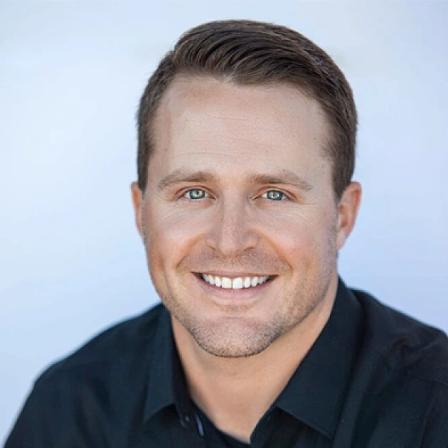 Professional headshot of smiling man in dark polo shirt against blue background for dental practice.