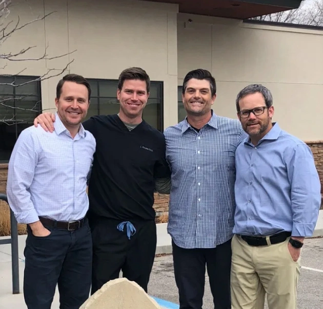 Four male dental professionals posing together in casual office setting.